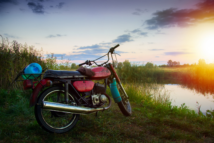 very old motorcycle traveler fisherman on the shore of a small river at sunset